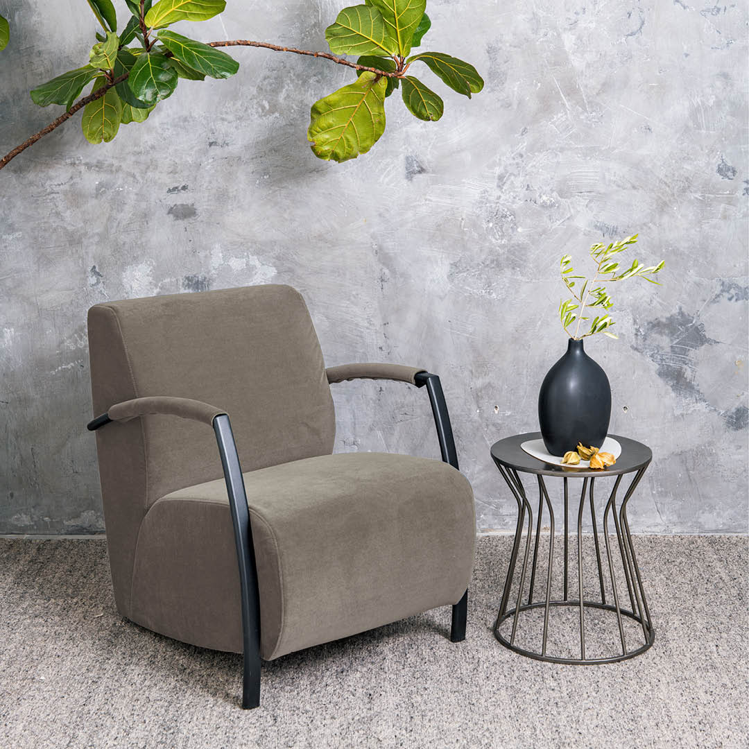 Fauteuil taupe avec accoudoirs en métal noir et revêtement robuste, idéalement assorti à une table d’appoint industrielle.