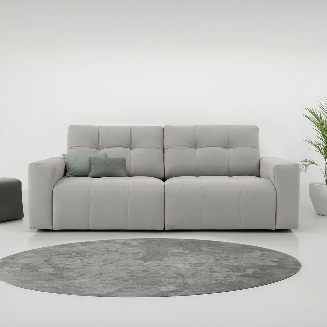 Lichtgrijze zetel met twee sierkussens in groenblauwe tinten op een rond grijs vloerkleed in een minimalistisch interieur