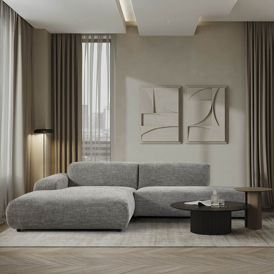 Lichtgrijze designhoekzetel met brede zitting en lage rugleuning, geplaatst in een elegante woonkamer met beige accenten.